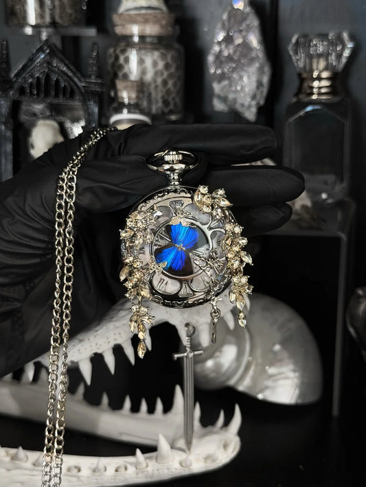 Lepidora Entomology blue gold pocket watch with intricate design and antique-style chain on a white background.